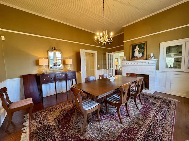 dining room featuring a brick fireplace, crown molding, a chandelier, a wainscoted wall, and wood finished floors