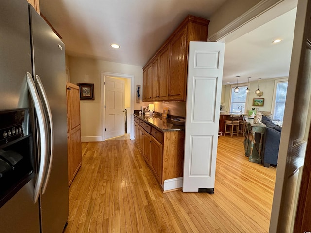 kitchen featuring dark countertops, recessed lighting, light wood-style floors, brown cabinetry, and stainless steel fridge with ice dispenser