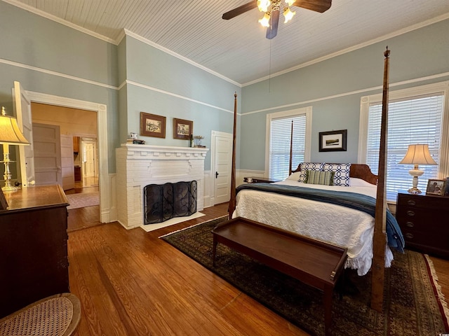 bedroom with ornamental molding, a brick fireplace, a ceiling fan, and wood finished floors