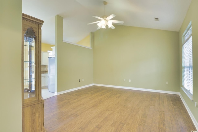 spare room featuring visible vents, baseboards, lofted ceiling, wood finished floors, and a ceiling fan