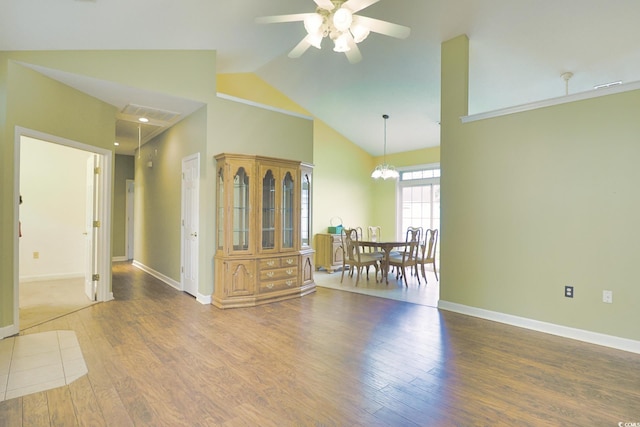 unfurnished room with high vaulted ceiling, ceiling fan with notable chandelier, wood finished floors, baseboards, and attic access