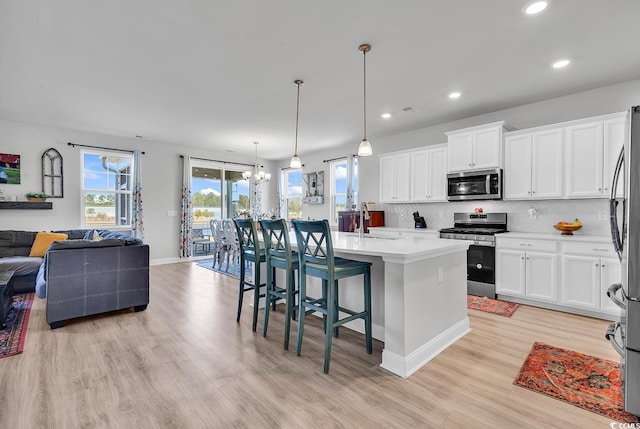 kitchen with open floor plan, decorative backsplash, appliances with stainless steel finishes, a notable chandelier, and a sink