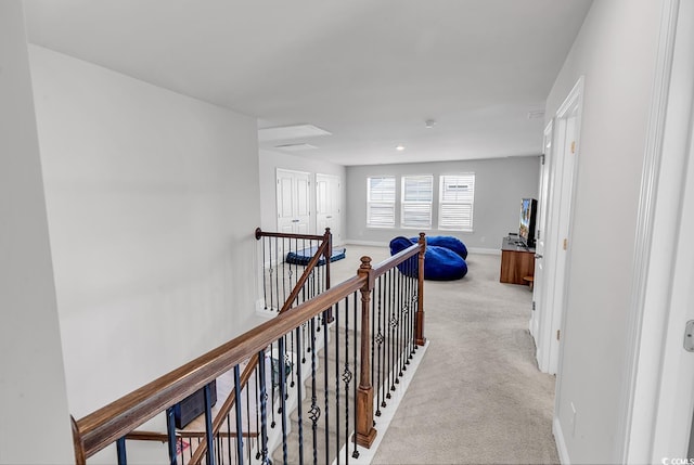 hallway featuring an upstairs landing, baseboards, and light carpet