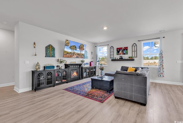 living area with wood finished floors, visible vents, baseboards, recessed lighting, and a glass covered fireplace