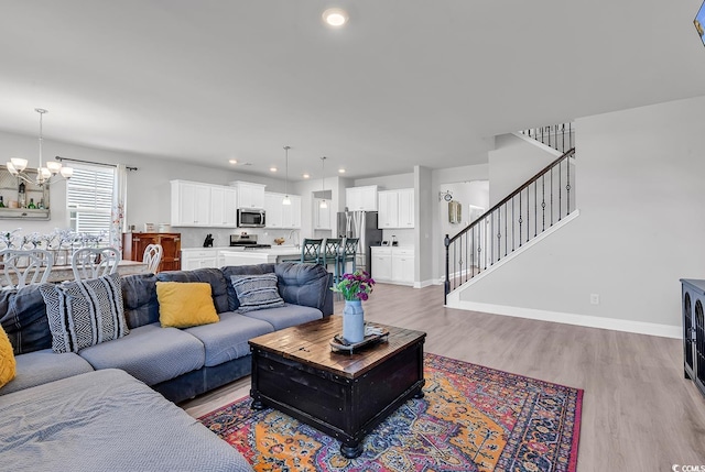 living room featuring baseboards, a notable chandelier, light wood-style flooring, and stairs