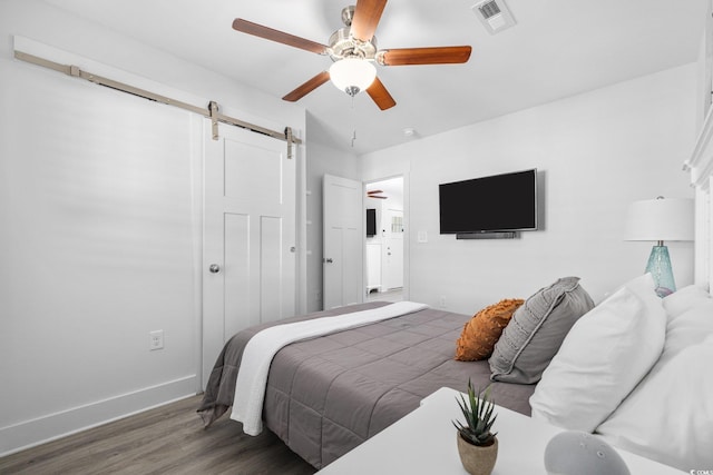 bedroom featuring visible vents, a ceiling fan, wood finished floors, a barn door, and a closet