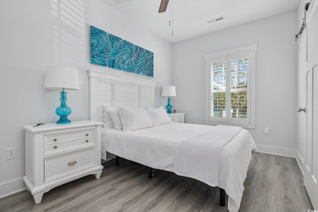 bedroom with light wood-type flooring, visible vents, a barn door, baseboards, and ceiling fan