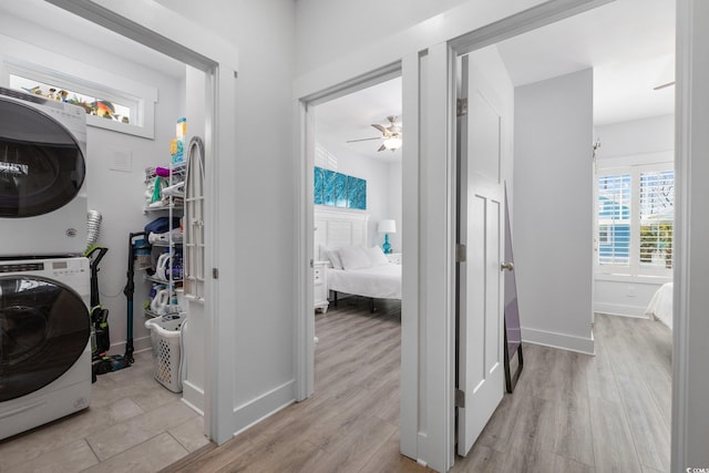 washroom with laundry area, stacked washer / dryer, light wood-type flooring, and baseboards