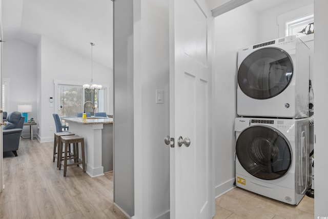 clothes washing area featuring light wood finished floors, stacked washer / dryer, baseboards, laundry area, and a notable chandelier