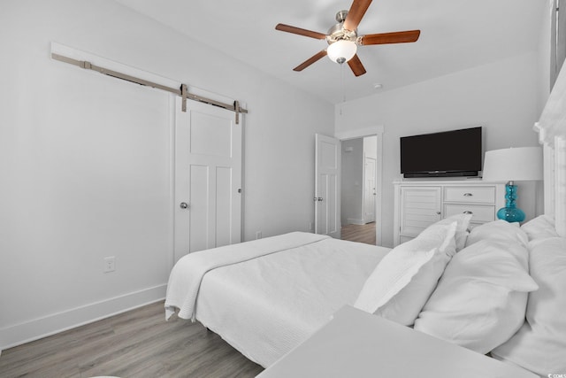 bedroom with baseboards, a ceiling fan, a barn door, and wood finished floors