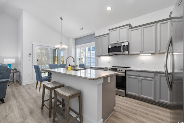 kitchen with gray cabinets, a sink, stainless steel appliances, lofted ceiling, and light stone countertops