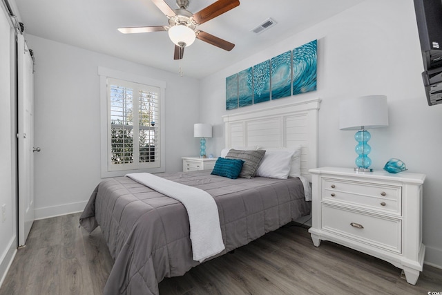 bedroom featuring visible vents, baseboards, a barn door, and wood finished floors