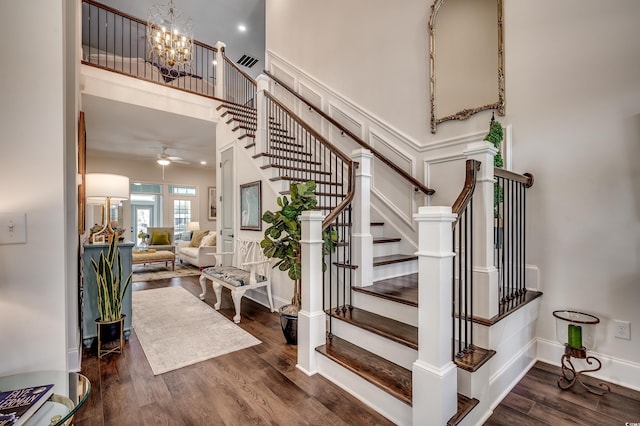 stairs featuring visible vents, ceiling fan with notable chandelier, wood finished floors, baseboards, and a towering ceiling