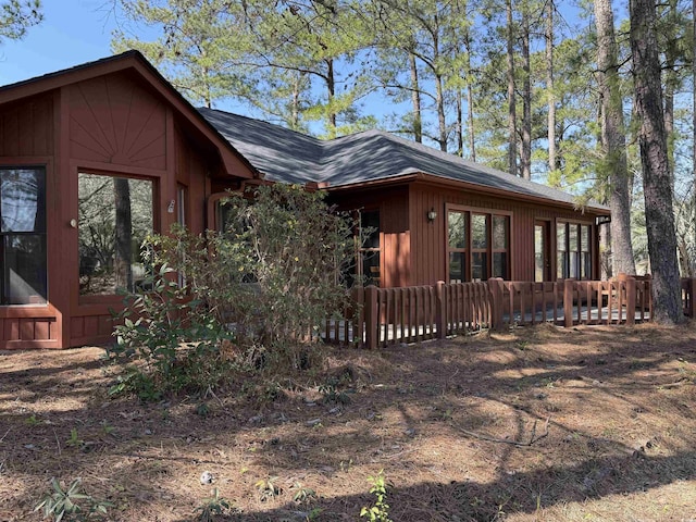 view of side of home featuring roof with shingles and fence