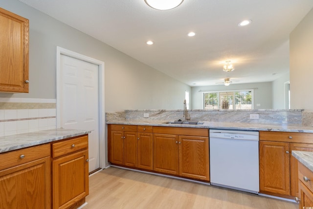 kitchen with a sink, brown cabinets, white dishwasher, and light stone countertops