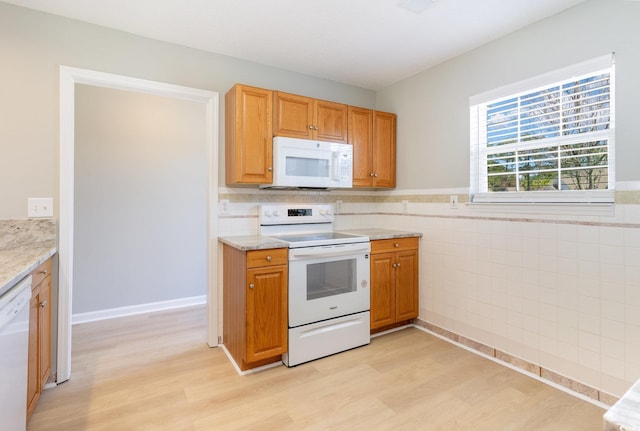 kitchen with light stone countertops, wainscoting, light wood-style floors, white appliances, and tile walls