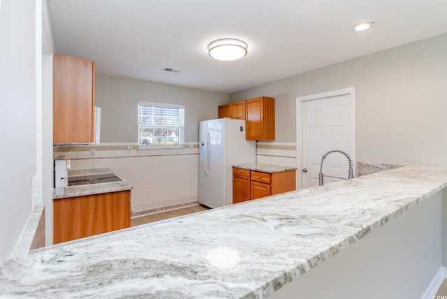 kitchen with brown cabinetry, visible vents, a peninsula, a sink, and white fridge with ice dispenser