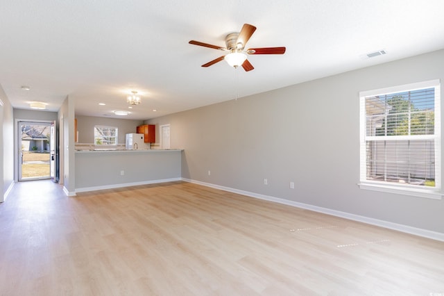 unfurnished living room featuring light wood finished floors, baseboards, and a wealth of natural light