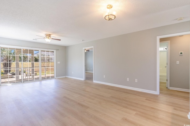 spare room featuring baseboards, a ceiling fan, light wood-type flooring, and a textured ceiling