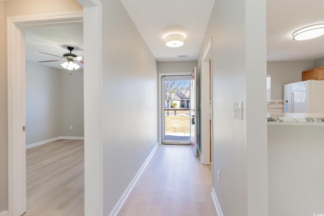 hallway featuring visible vents, a textured ceiling, light wood-style floors, and baseboards