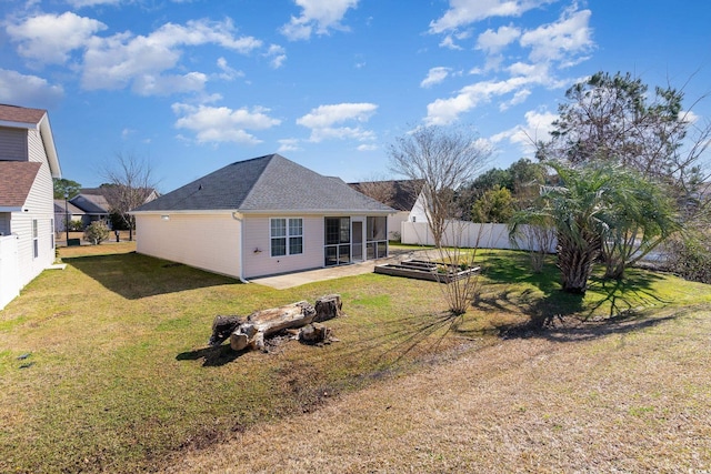 back of house featuring a lawn, a shingled roof, fence, a sunroom, and a garden