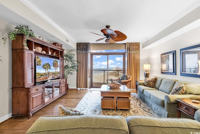 living area featuring a ceiling fan, baseboards, wood finished floors, visible vents, and ornamental molding