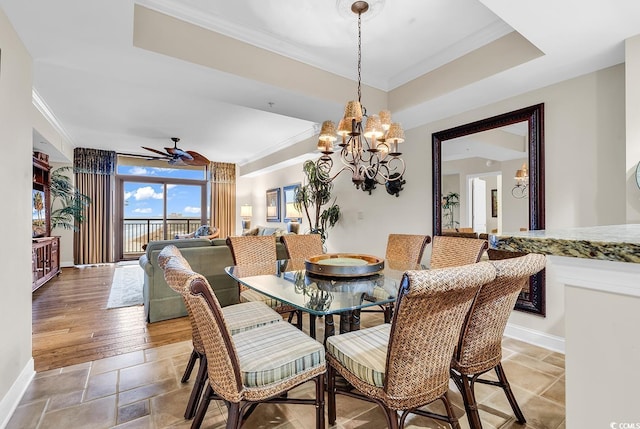 dining room featuring ceiling fan with notable chandelier, a tray ceiling, stone tile floors, crown molding, and baseboards