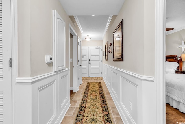 hall with a decorative wall, crown molding, and a wainscoted wall