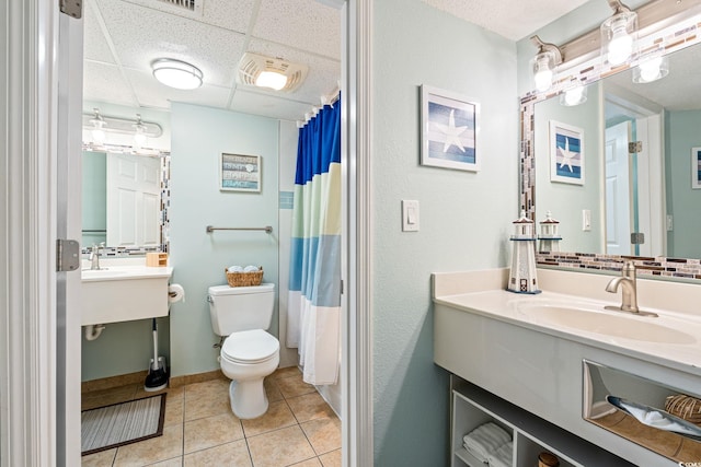 bathroom featuring tile patterned flooring, tasteful backsplash, toilet, a paneled ceiling, and a sink