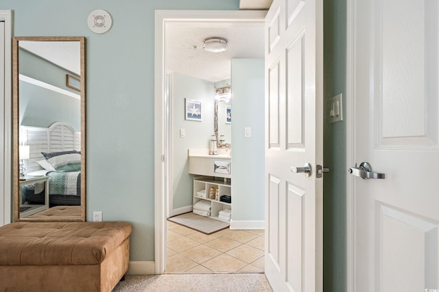 corridor with light tile patterned floors, light colored carpet, baseboards, and a textured ceiling