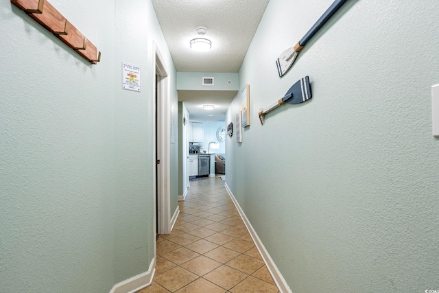 corridor with light tile patterned floors, visible vents, a textured ceiling, and baseboards