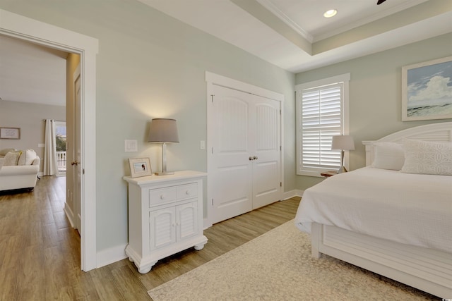 bedroom featuring a tray ceiling, baseboards, and light wood-style floors