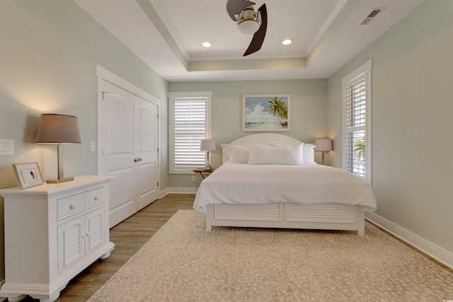 bedroom with a tray ceiling, multiple windows, baseboards, and wood finished floors