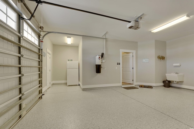 garage with a garage door opener, freestanding refrigerator, baseboards, and a sink