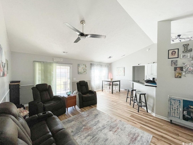 living room featuring a ceiling fan, baseboards, visible vents, vaulted ceiling, and light wood-type flooring