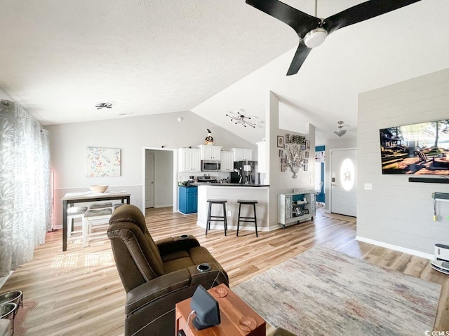 living room with vaulted ceiling, a ceiling fan, light wood-type flooring, and a textured ceiling