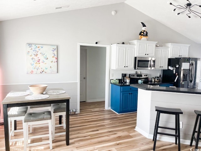 kitchen with a breakfast bar, dark countertops, stainless steel appliances, white cabinets, and light wood finished floors