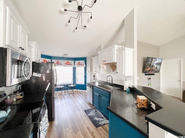 kitchen with a peninsula, a sink, stainless steel appliances, white cabinets, and dark countertops