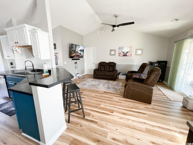 kitchen with a sink, white cabinetry, dark countertops, a kitchen breakfast bar, and light wood-type flooring