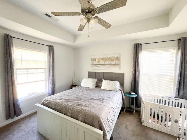 bedroom featuring visible vents, a raised ceiling, a ceiling fan, and carpet flooring