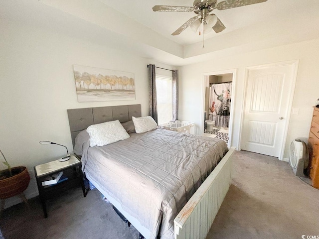 bedroom featuring a raised ceiling, carpet, ensuite bathroom, and ceiling fan