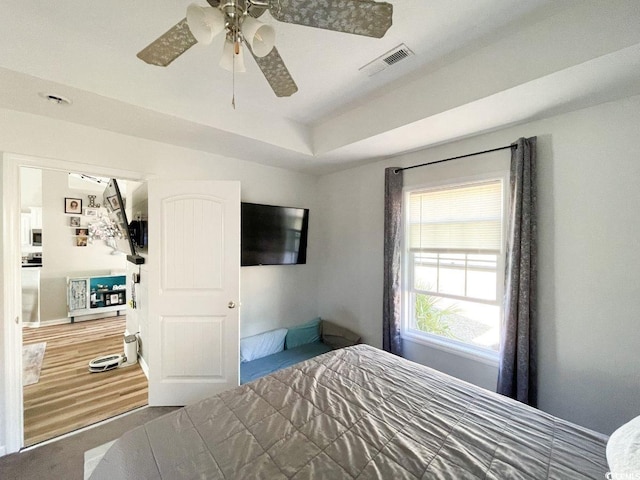 bedroom featuring a tray ceiling, wood finished floors, visible vents, and ceiling fan