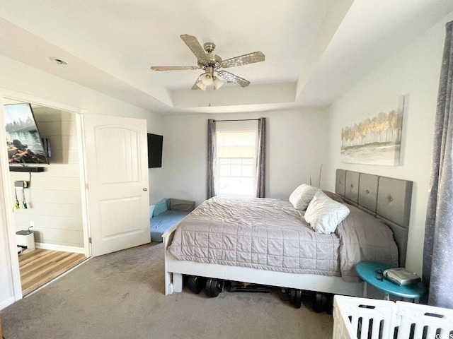 carpeted bedroom with a raised ceiling and ceiling fan