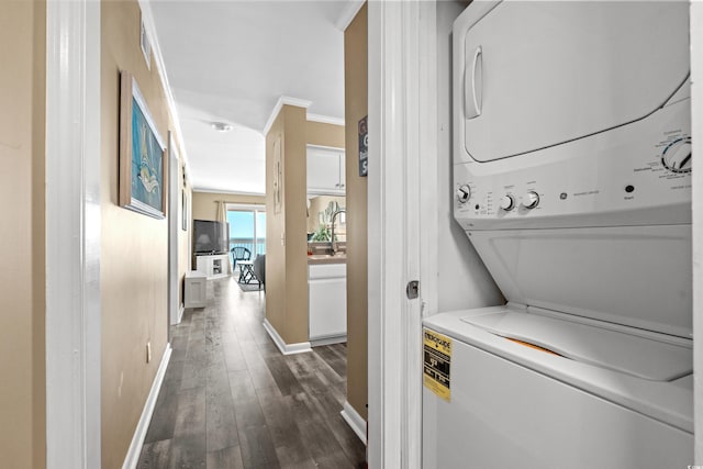 clothes washing area with crown molding, baseboards, dark wood finished floors, laundry area, and stacked washing maching and dryer