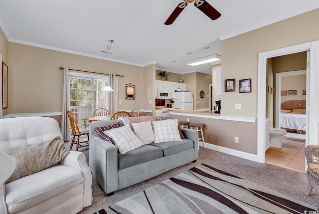 living room featuring ornamental molding, a ceiling fan, light tile patterned floors, baseboards, and light colored carpet