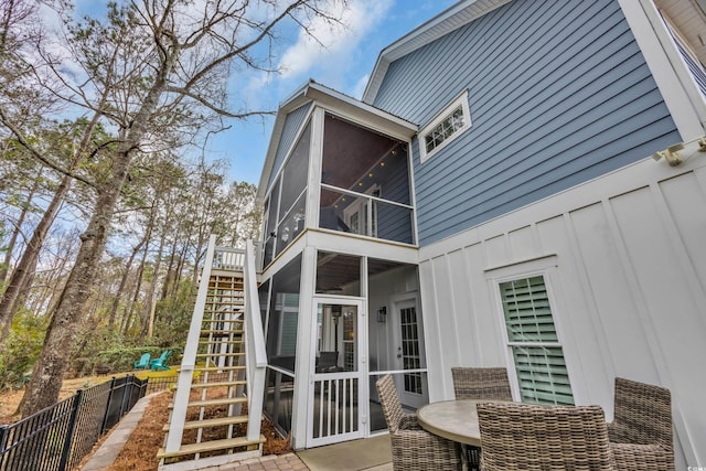 back of house with board and batten siding, fence, stairway, a sunroom, and a patio area