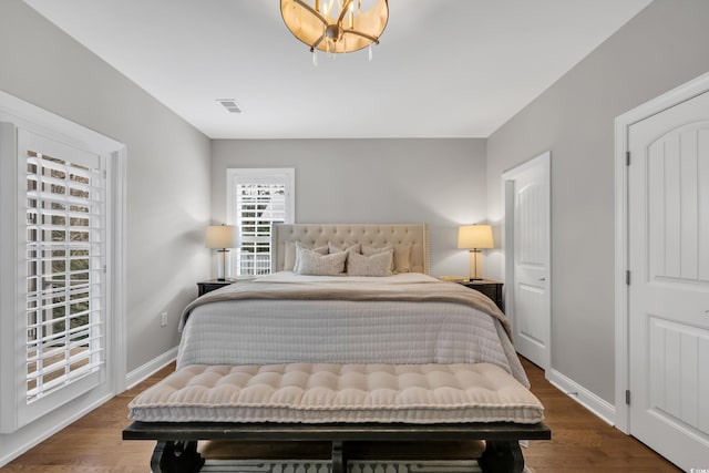 bedroom with visible vents, baseboards, a notable chandelier, and wood finished floors