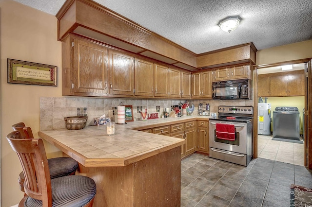 kitchen featuring electric stove, electric water heater, tile countertops, a peninsula, and black microwave