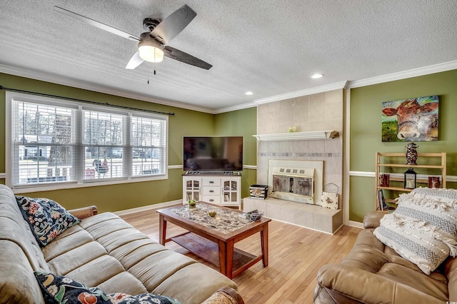 living room featuring light wood finished floors, a tiled fireplace, ceiling fan, and ornamental molding