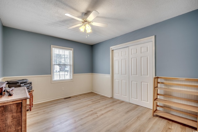 bedroom with a closet, light wood-style floors, wainscoting, and a textured ceiling